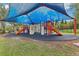 Well-equipped playground with slides, climbing walls, and play structures under a blue sunshade at 4235 Prima Lago Dr, Lakeland, FL 33810