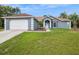 Front view of a one-story gray home featuring a two car garage, a well-manicured lawn and mature trees at 8628 Sw 133Rd Lane Rd, Ocala, FL 34473