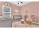 Cozy Bedroom featuring soft pink walls, a crib, a rocking chair, and natural light from the window at 2359 White Cedar Way, Haines City, FL 33844