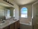 Bathroom with a double sink vanity, tiled bathtub, and arched window for natural light at 103 Thornbush Pkwy, Davenport, FL 33837