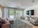 Open-concept living room with gray rug, plush sofa, TV, balcony access, and plenty of natural light at 67 Bella Oaks Dr, Port Orange, FL 32129