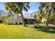 Charming home with a screened-in porch, lush lawn, and white exterior, surrounded by tropical palm trees and green foliage at 1437 Colin Kelly Ave, Daytona Beach, FL 32124