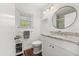 Bright bathroom with white vanity, granite countertop, round mirror, and window with blinds at 1401 S Palmetto Ave # 614, Daytona Beach, FL 32114