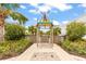 Paradise Pool entrance with a rustic wooden gate, lush tropical foliage and stone pavers under sunny blue skies at 562 Landshark Blvd, Daytona Beach, FL 32124