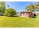 Home's backyard featuring a brick exterior, lush lawn, mature trees, and a screened pool area at 953 Pineapple Rd, South Daytona, FL 32119
