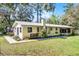 Back of the single-story home with mature trees, well-kept lawn, and a glimpse of the screened porch at 53722 Rivertrace Rd, Astor, FL 32102