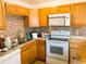 Functional kitchen with wood cabinets, mosaic backsplash, and white appliances providing a practical cooking space at 5076 Fairport Ave, De Leon Springs, FL 32130