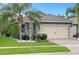 Landscaped front yard with green grass, palm trees, and brick-paved driveway leading to the home's two-car garage at 214 Caryota Ct, New Smyrna Beach, FL 32168
