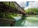 A picturesque metal bridge spans over crystal-clear waters, framed by green trees under a partly cloudy sky at 26 E Kelly Park Rd, Apopka, FL 32712