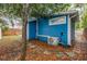 Side view of the blue house with an AC unit surrounded by mature trees and a leaf-covered yard at 205 Mary Ave, New Smyrna Beach, FL 32168