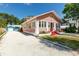 Charming pink home with red steps and a gravel driveway, surrounded by lush greenery under a clear blue sky at 205 Mary Ave, New Smyrna Beach, FL 32168