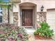 Inviting entryway with a solid wood door and stone accents framed by lush, vibrant landscaping at 30029 Pga Dr, Sorrento, FL 32776