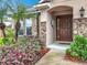 Inviting entryway with a solid wood door and stone accents framed by lush, vibrant landscaping at 30029 Pga Dr, Sorrento, FL 32776