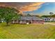 Charming single story brick home with a large lawn and mature tree, under a colorful sky at 3104 Umbrella Tree Dr, Edgewater, FL 32141