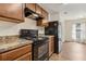 Galley kitchen featuring wood cabinets, granite countertops, and black appliances at 3845 Arborvitae Way, Deland, FL 32724