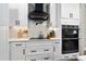 Well-equipped kitchen featuring a black range hood, cooktop, white cabinets, subway tile, and built-in double ovens at 1015 Tallacoe Trl, New Smyrna Beach, FL 32168
