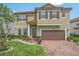 Two-story home featuring a red-tiled roof, brown shutters, a two-car garage, and a brick driveway with landscaping at 199 Verde Way, Debary, FL 32713