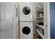 A stacked white washer and dryer with shelving to the side is located in the laundry room at 241 Riverside Dr # 1909, Daytona Beach, FL 32117