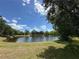 Scenic view of a serene pond surrounded by lush green grass and mature trees under a clear blue sky at 319 E Victoria Trails Blvd, Deland, FL 32724