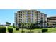 A yellow exterior condominium building with white balconies surrounded by green grass and palm trees on a bright, sunny day at 4670 Links Village Dr # B102, Ponce Inlet, FL 32127