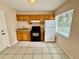 Compact kitchen with wooden cabinets, a white refrigerator, tile floors, and natural light from the window at 111 S Delaware Ave, Deland, FL 32720