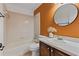 Bathroom with vanity, tiled tub-shower, round mirror, and an orange accent wall at 2704 Lancaster Ct, Apopka, FL 32703