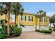 Yellow townhome featuring a two-car garage, green shutters and lush tropical landscaping at 2982 S Atlantic Ave, New Smyrna Beach, FL 32169