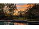 Backyard view of an in-ground pool with iron fencing, and a beautiful sunset with orange and yellow hues at 150 Lake Charles Rd, Deland, FL 32724