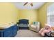 Bright yellow bedroom with ceiling fan, a blue crib, a glider, and a side table at 2337 Oxmoor Dr, Deland, FL 32724
