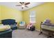 Bright yellow bedroom with ceiling fan, a blue crib, a glider, and a side table at 2337 Oxmoor Dr, Deland, FL 32724