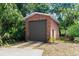 Detached brick garage nestled in lush greenery featuring a gray door, providing ample space for vehicles or storage at 6185 Shoreline Dr, Port Orange, FL 32127