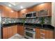 Stylish kitchen featuring stainless steel appliances, wood cabinetry, and mosaic tile backsplash at 231 Riverside Dr # 2310, Holly Hill, FL 32117