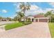 Beautiful home featuring a brick driveway, lush landscaping, and tall palm trees under a bright, cloudy sky at 2811 S Asciano Ct, New Smyrna Beach, FL 32168