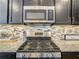 Close-up of kitchen gas range with stainless steel hood, mosaic backsplash and granite countertops at 260 Teddy Rushing St, Debary, FL 32713
