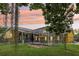A backyard view of a caged pool with a fenced yard during sunset, featuring lush green grass and mature trees at 2940 Se 23Rd Ave, Ocala, FL 34471