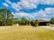 Expansive front yard with a single-story home, wooden storage units, and a backdrop of lush trees at 7380 Orange Ave, Indian Lake Estates, FL 33855