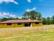 Single-story home features a lush front lawn, and is set against a backdrop of mature trees at 7380 Orange Ave, Indian Lake Estates, FL 33855
