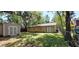 The backyard shows the exterior of a tan home and a matching shed surrounded by mature trees at 1621 Anniston Ave, Daytona Beach, FL 32117