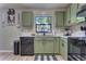 Well-lit kitchen with sage-green cabinets, black appliances, and hardwood floors offers an efficient layout at 348 Southern Winds Blvd, Deland, FL 32720