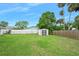 Spacious backyard featuring lush green grass, white fence, storage shed, and mature palm trees at 718 Sleepy Hollow Dr, Port Orange, FL 32127