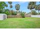 Spacious backyard featuring lush green grass, a wooden fence, storage shed, and mature palm trees at 718 Sleepy Hollow Dr, Port Orange, FL 32127