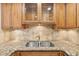 Close up of kitchen sink featuring granite countertops, wood cabinetry with glass doors, and a tile backsplash at 2987 S Atlantic Ave # 903, Daytona Beach, FL 32118