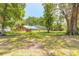 Wide view of backyard with a brick home, pool enclosure, mature trees and lush green grass at 712 S Timberlane Dr, New Smyrna Beach, FL 32168