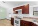 A cozy kitchen features dark wood cabinetry, neutral countertops, and white appliances under a bright window at 1018 E Gaucho Cir, Deltona, FL 32725