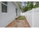 View of the side yard showing the exterior wall of the house, grass, mulch, and a white vinyl fence at 1094 Lolita St, Orange City, FL 32763