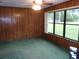 Living room featuring wood paneling, a ceiling fan, green carpet, and a large window at 871 Oak Tree Ln, Lake Helen, FL 32744