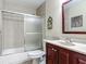 Bathroom features a shower-tub combo with glass doors, tile surround, vanity with sink, and cherry colored cabinets at 1516 Arrowhead Trl, Enterprise, FL 32725
