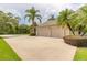 Three-car garage with a concrete driveway, lush landscaping, and mature palm trees at 15 Cambridge Trce, Ormond Beach, FL 32174