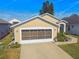 Tan one-story house with white garage door, landscaping, and paved driveway at 152 Travis Ln, Davenport, FL 33837