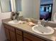 Bathroom with a double vanity, wood cabinets, and a large mirror reflecting the bedroom at 2595 Edenville Path, The Villages, FL 32162